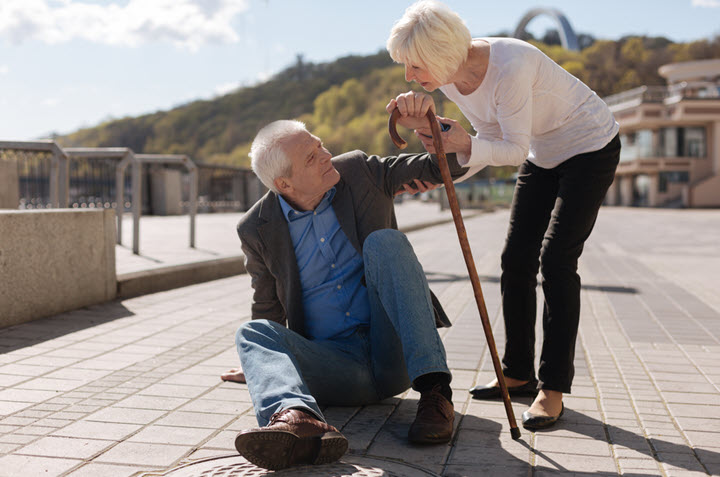 active senior couple outdoors and woman is helping man with cane up from ground